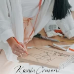 Fashion designer sketching a garment on brown paper with a red marker among sewing tools and measuring tape.