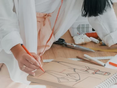 Fashion designer sketching a garment on brown paper with a red marker among sewing tools and measuring tape.